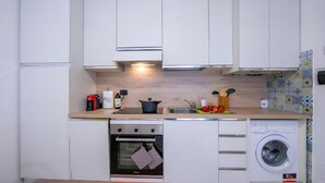 A compact kitchen with white cabinets, a built-in oven, a washing machine, and a coffee maker.