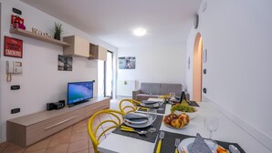 A modern living room with a TV, sofa, and dining area with yellow chairs and a table set for two.