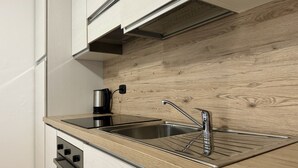 A kitchen with a stainless steel sink, a kettle, and wooden cabinetry.
