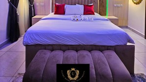 Un dormitorio moderno con una cama grande, lámparas de noche y una luz decorativa en la pared.