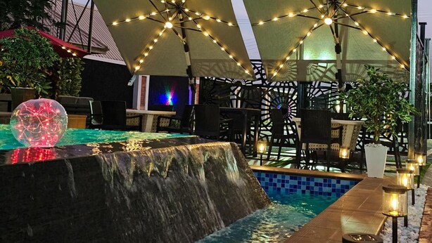 Zona de piscina exterior con cascada, asientos y luces colgantes.