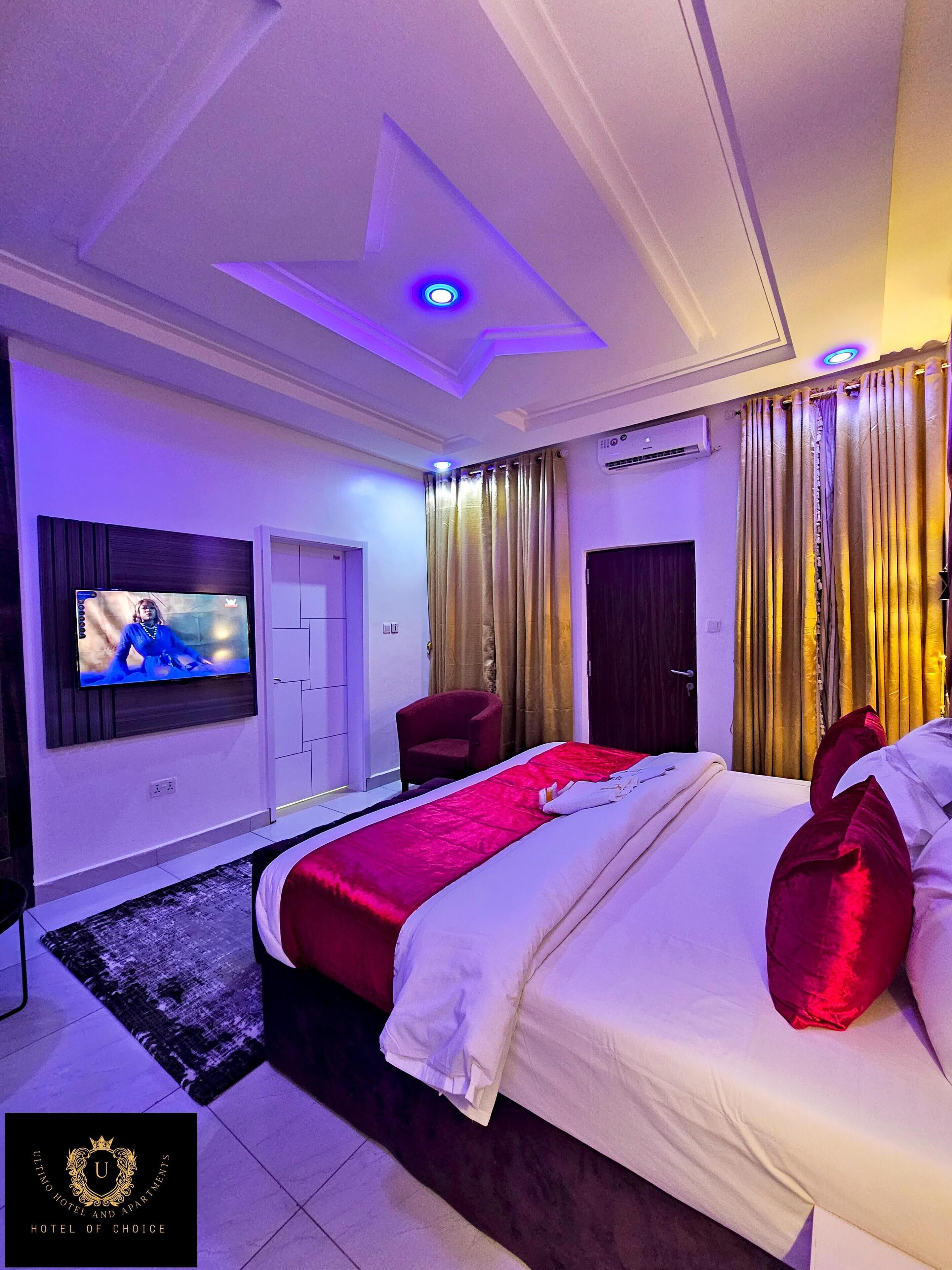 A hotel bedroom with a bed, a TV, a chair, and curtains.