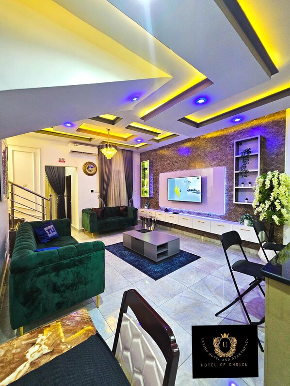 A modern living room with a green sofa, a coffee table, and a TV mounted on the wall. - 2 Bed Apartment 3 - Bright Benin City Stay (Benin City)