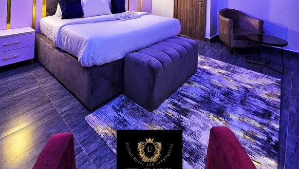 A modern bedroom with a large bed, a seating area, and a painting on the wall. - 2 Bed Apartment 1 - Stylish Benin City Retreat (Benin City)