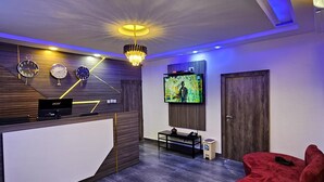 Un moderno vestíbulo de hotel con un mostrador de recepción, una pantalla de televisión, un sillón de terciopelo rojo y una araña.