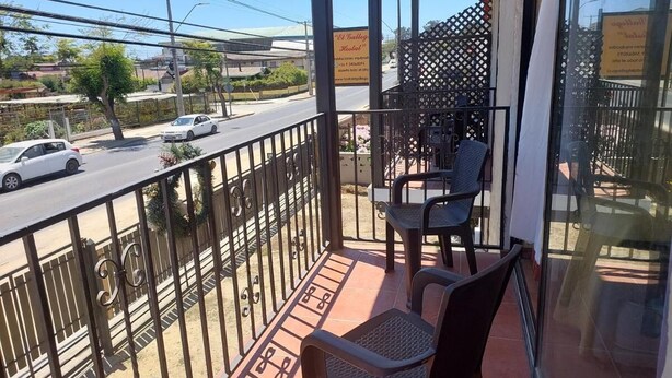 Un balcon avec deux chaises, une balustrade et une vue sur une rue où circulent des voitures.