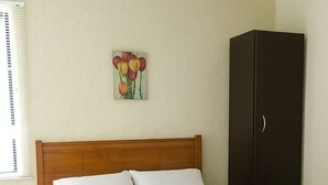Une chambre à coucher avec une tête de lit en bois, du linge de lit blanc, une table de chevet, une armoire et un tableau représentant des tulipes accroché au mur.