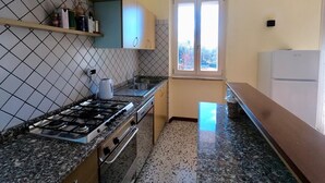 A kitchen with a gas stove, oven, and sink. There is a window with a view of trees outside.