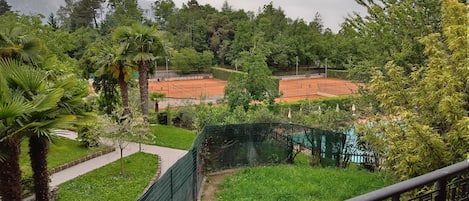 Una cancha de tenis rodeada de exuberante vegetación y con montañas al fondo.