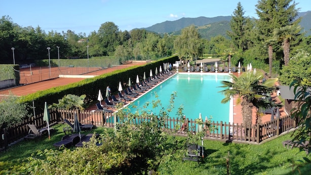 A swimming pool with sun loungers and umbrellas, surrounded by greenery and a wooden fence.