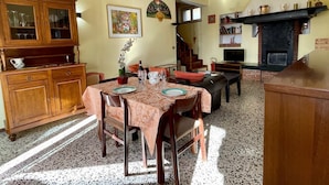 A dining area with a table set for four, a wooden cabinet with glass doors, a fireplace, and a staircase leading to another room.
