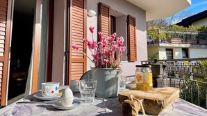 A balcony with a table set for breakfast, including plates, cups, and a jar of olive oil.