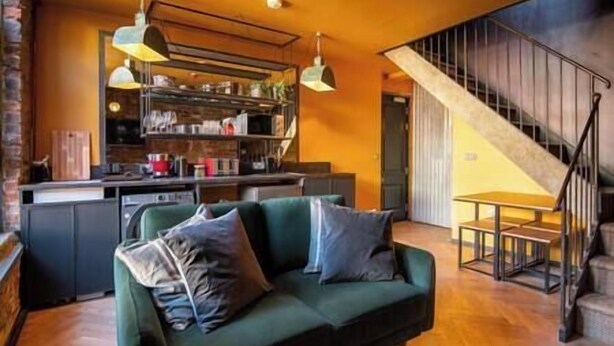 A modern kitchen with a dining area, featuring a green sofa with cushions, a staircase, and pendant lighting. - Terrace View · City Centre Modern Apartment (West Yorkshire)