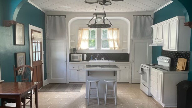 Una cocina con armarios blancos, una isla central con taburetes, un microondas y una estufa.