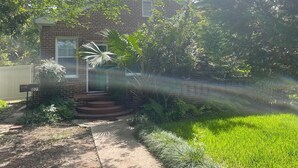 Una casa de ladrillo con un porche delantero, un buzón y un jardín bien cuidado con diversas plantas y césped.