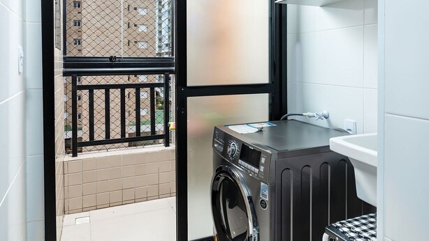 Une petite buanderie comprenant un lave-linge, un petit tabouret et donnant sur un balcon agrémenté d’une balustrade.