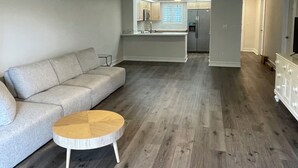 Ein modernes Wohnzimmer mit einem grauen Sofa, einem Holztisch und einer Küche im Hintergrund.