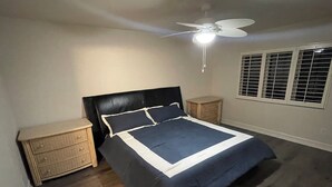Ein Schlafzimmer mit einem Bett, zwei Nachttischen, einem Deckenventilator und einem Fenster mit Jalousien.
