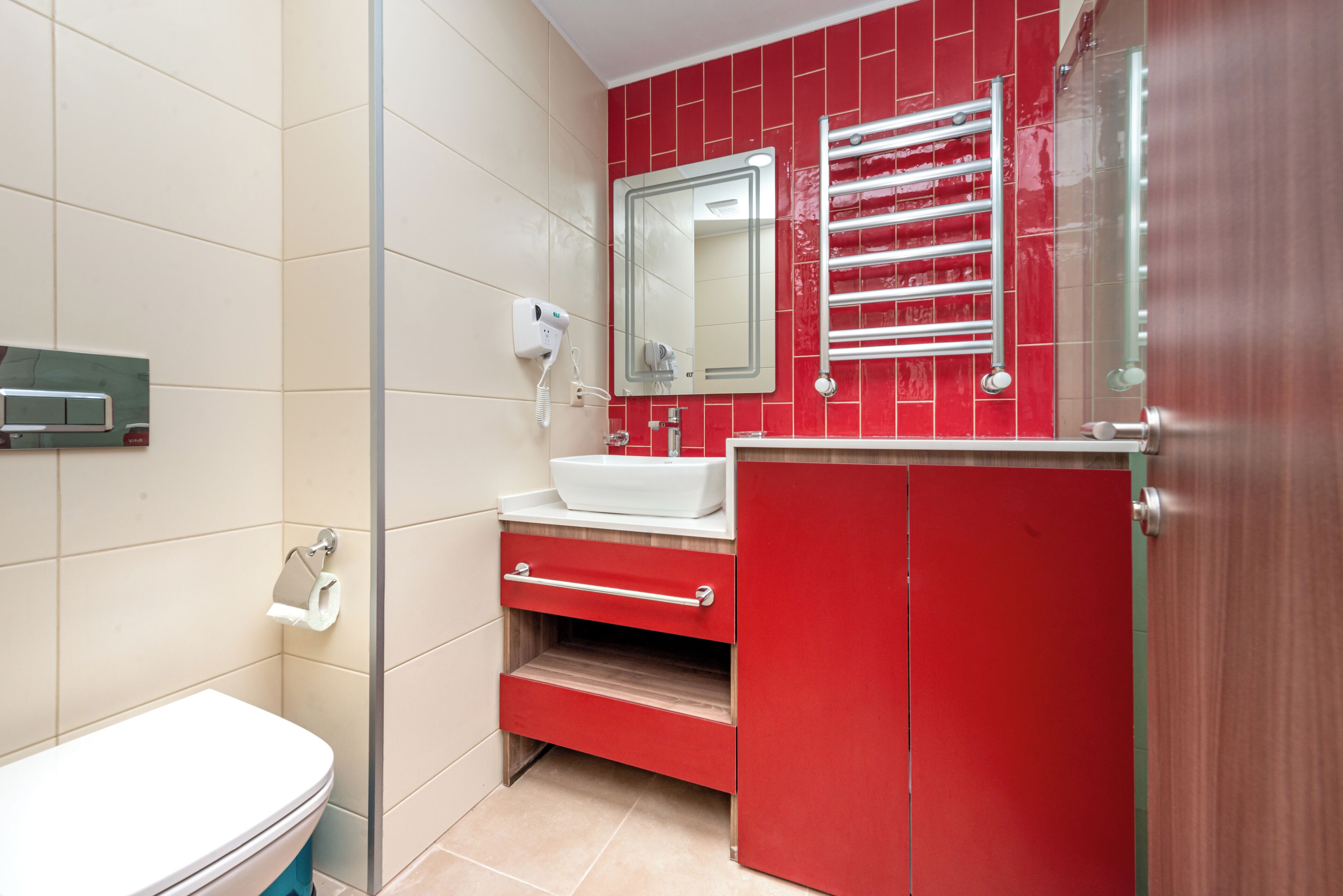 Um banheiro com vaso sanitário branco, toucador vermelho, espelho e porta-toalhas.