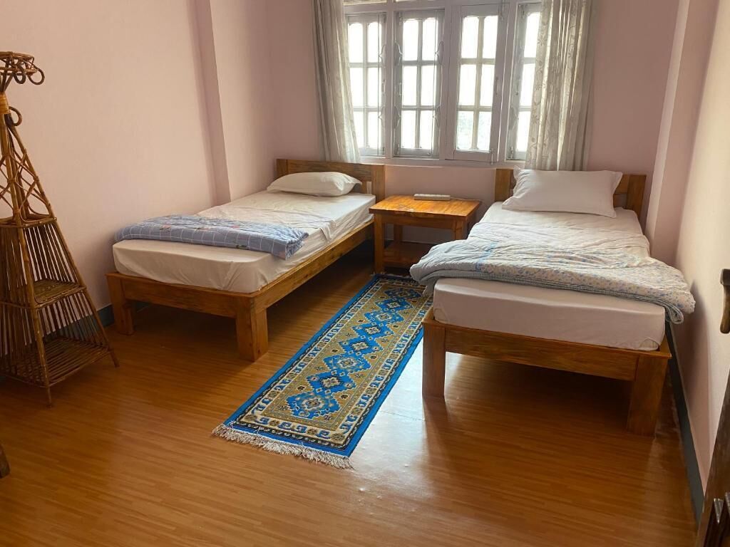 Une pièce avec deux lits en bois, une petite table en bois, un tapis bleu à motifs et une chaise en osier.