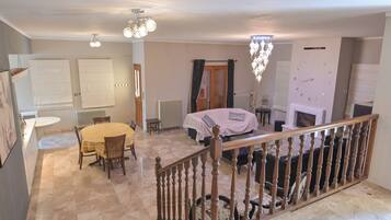 A spacious living area with a dining table, chairs, a fireplace, and a staircase with a wooden railing.