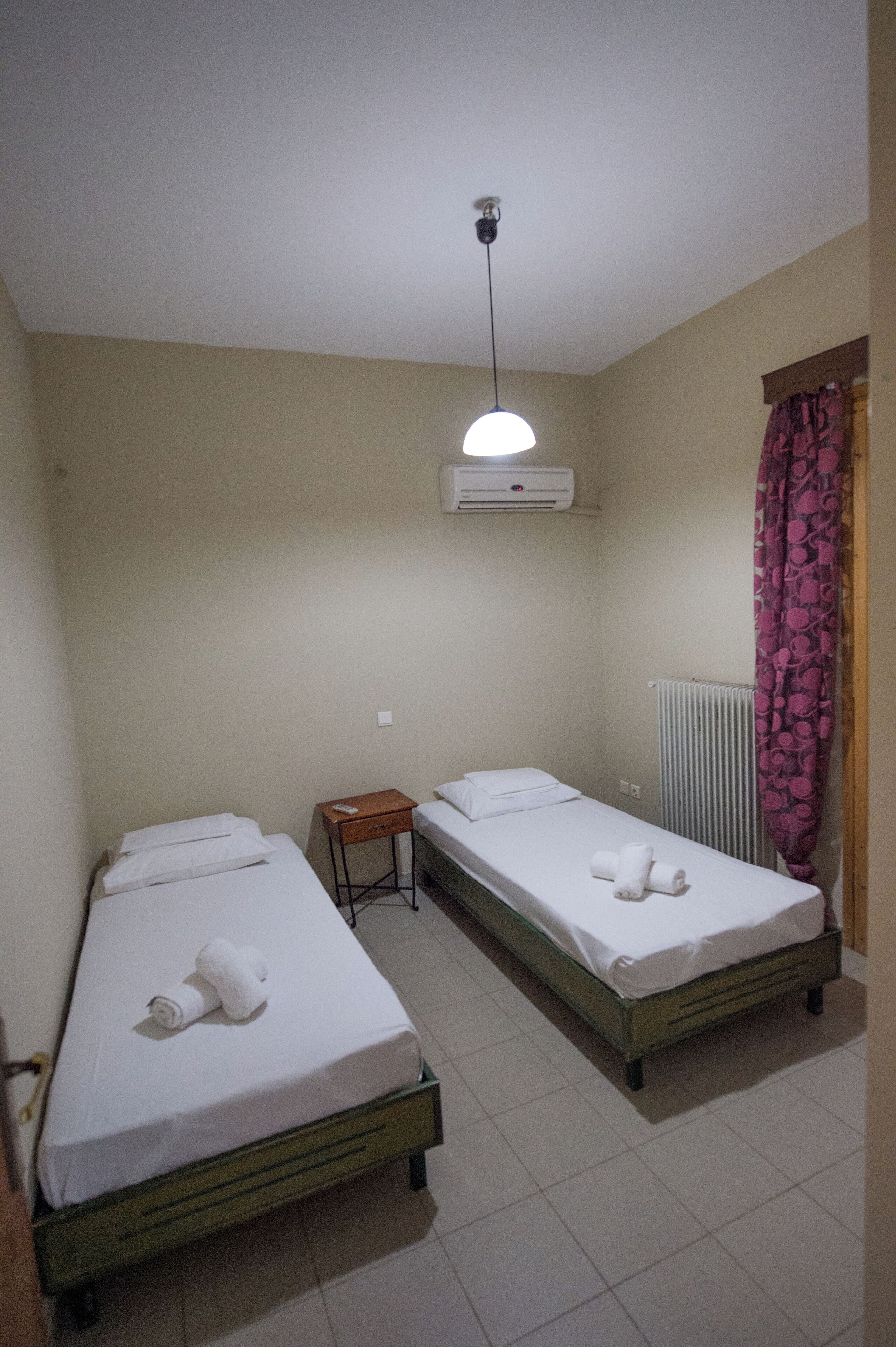 Une chambre double avec deux lits simples, une petite table, un appareil de climatisation et un radiateur.