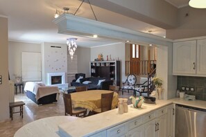 A spacious living area with a fireplace, a dining table, and a kitchen with white cabinets. - Thimeli (Epidaurus)