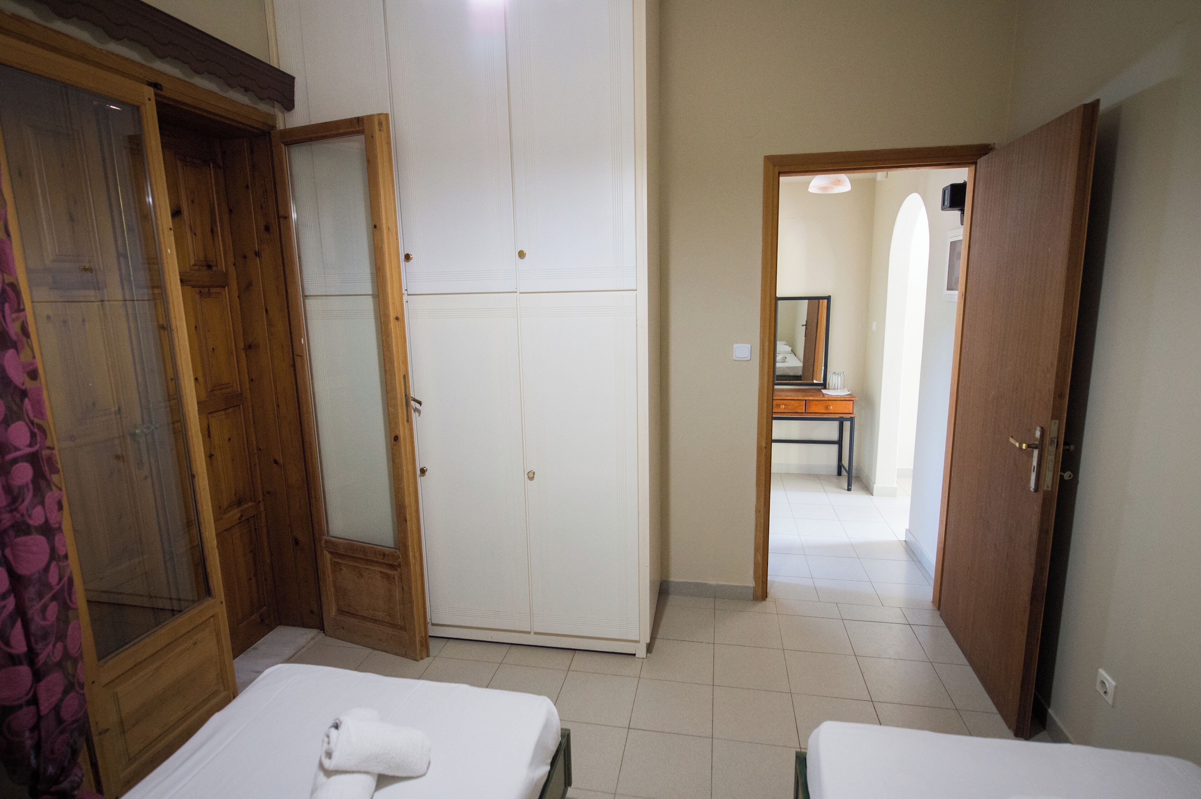 A bedroom with two beds, a wardrobe, and a bathroom visible through an open door.