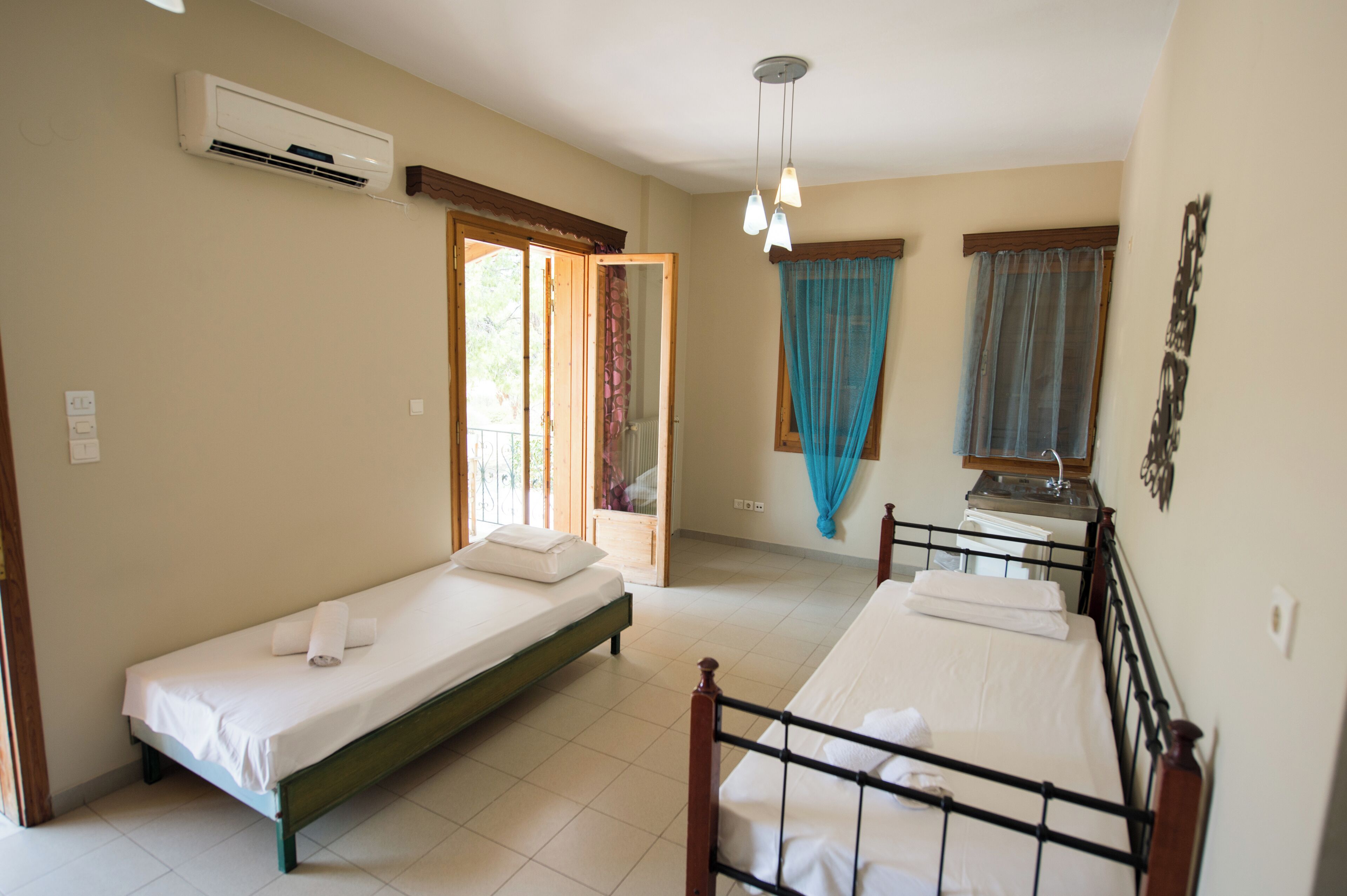 Une chambre avec deux lits simples, un appareil de climatisation, une fenêtre avec des rideaux et un luminaire au plafond.