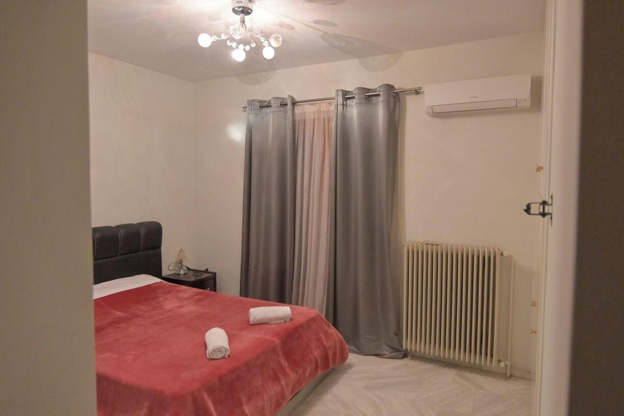 A bedroom with a bed, a nightstand, a radiator, and curtains.