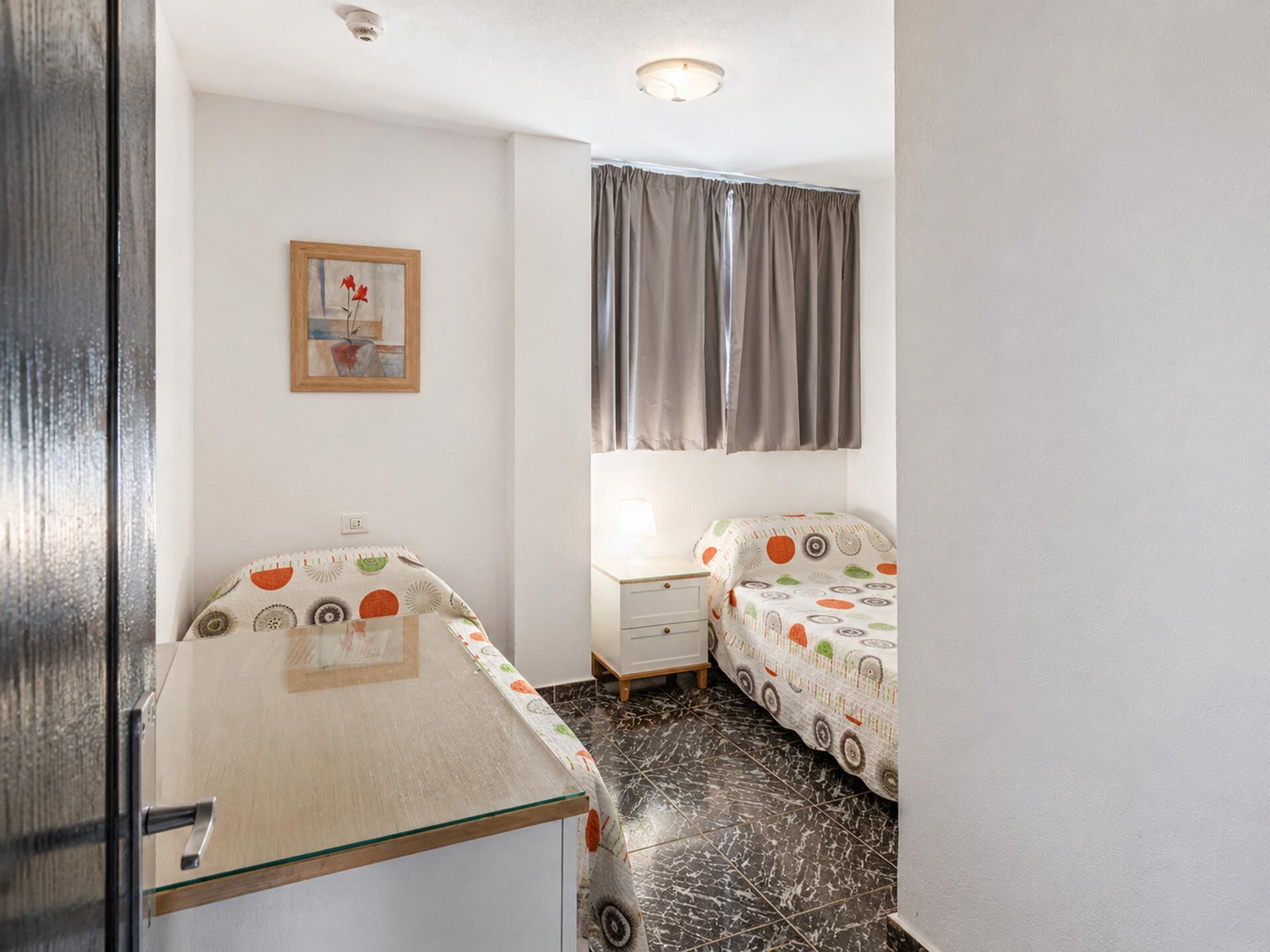A small, compact room with a bed, bedside table, and a wall-mounted picture.