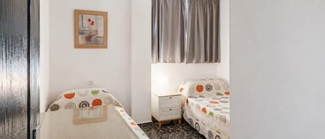 A small, compact room with a bed, bedside table, and a wall-mounted picture.