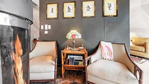 Una sala de estar acogedora con chimenea, dos sillones, una mesita auxiliar con lámpara y cuadros enmarcados en la pared.