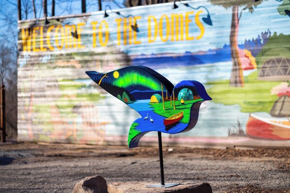 A colorful sign with a bird illustration and the text "WELCOME TO THE DOMES" in the background.