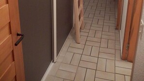 Un estrecho pasillo con una escalera de madera que lleva a una habitación con puerta corredera. Se ve una silla y una pequeña mesa al fondo.