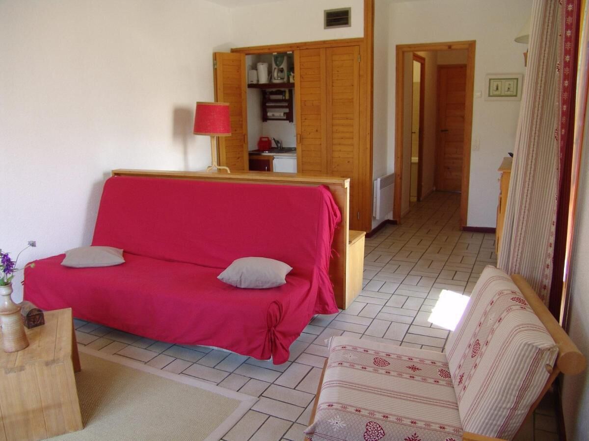 A cozy room with a red sofa, a patterned armchair, a wooden cabinet, and a small table with a vase.