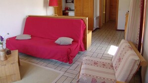Un cuarto acogedor con un sofá rojo, un sillón estampado, un armario de madera y una mesita con un jarrón.