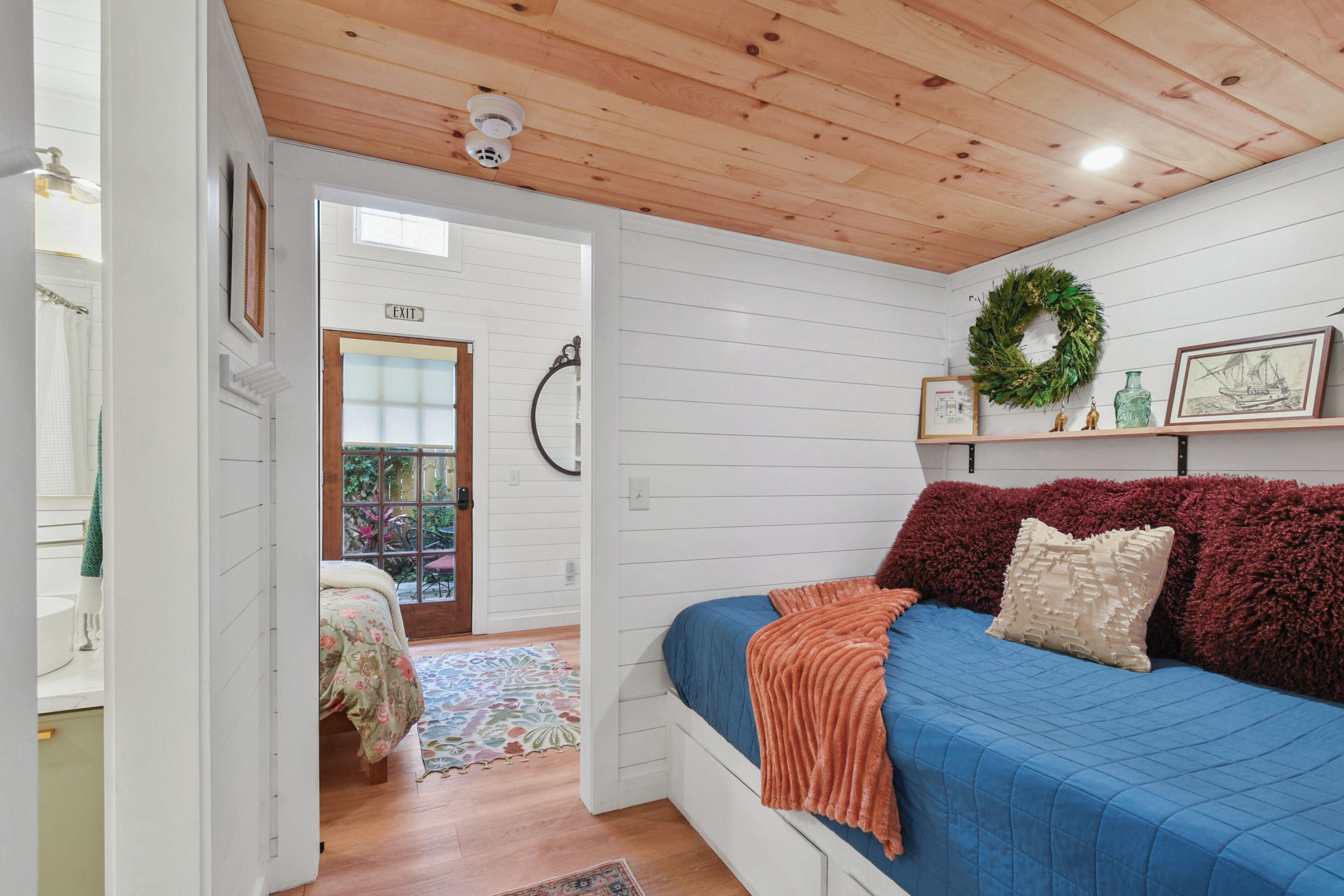 A bedroom with a bed, a wooden ceiling, a window, and a door leading to a balcony.
