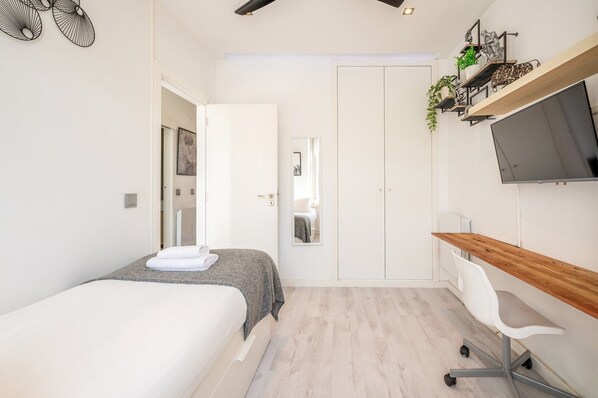 Une chambre à coucher moderne, équipée d’un lit, d’un bureau, d’une chaise et d’un téléviseur fixé au mur.