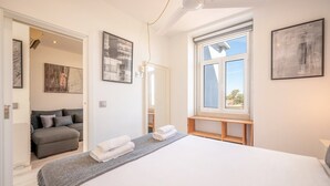 A modern bedroom with a large bed, a grey sofa, and a window with a view.