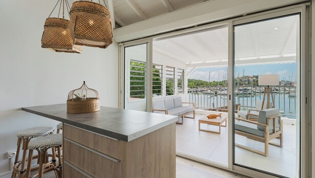 A modern kitchen with a large island, wicker hanging lights, and a view of a marina through large sliding doors. - Cosy, refurbished apartment, marina view (Le Gosier)