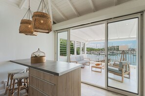 Une cuisine moderne dotée d'un grand îlot central, de luminaires suspendus en osier et offrant une vue sur une marina grâce à de grandes portes coulissantes.