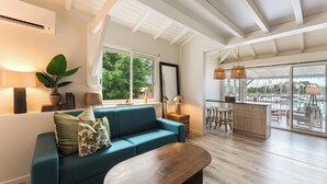 A spacious living area with a teal sofa, wooden coffee table, and a view of a marina through large glass doors. - Cosy, refurbished apartment, marina view (Le Gosier)