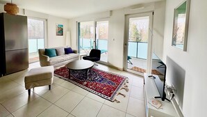 Een moderne woonkamer met een bank, een salontafel en een vloerkleed. Er is een balkon met een blauwe leuning en een stoel.