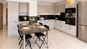 Een moderne keuken met grijze kastjes, een roestvrijstalen koelkast en een eettafel voor vier personen.