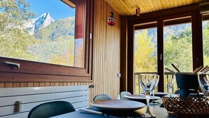 Et spiseområde med et bord dækket til to, udsigt til bjerge gennem store vinduer, og et træloft.
