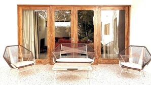Ein Zimmer mit einer großen Schiebeglasdoor, die auf einen Balkon führt, zwei Korbstühle und einem kleinen Tisch.