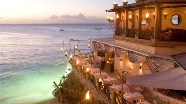 Ein Restaurant im Freien mit Tischen und Stühlen mit Blick auf das Meer.