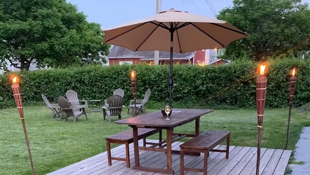 Une terrasse extérieure avec une table et des bancs en bois, entourée de chaises, et deux torches allumées.