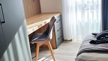 Ein Hotelzimmer mit Bett, Schreibtisch, Stuhl, Wandfernseher und einem Vorhangfenster.